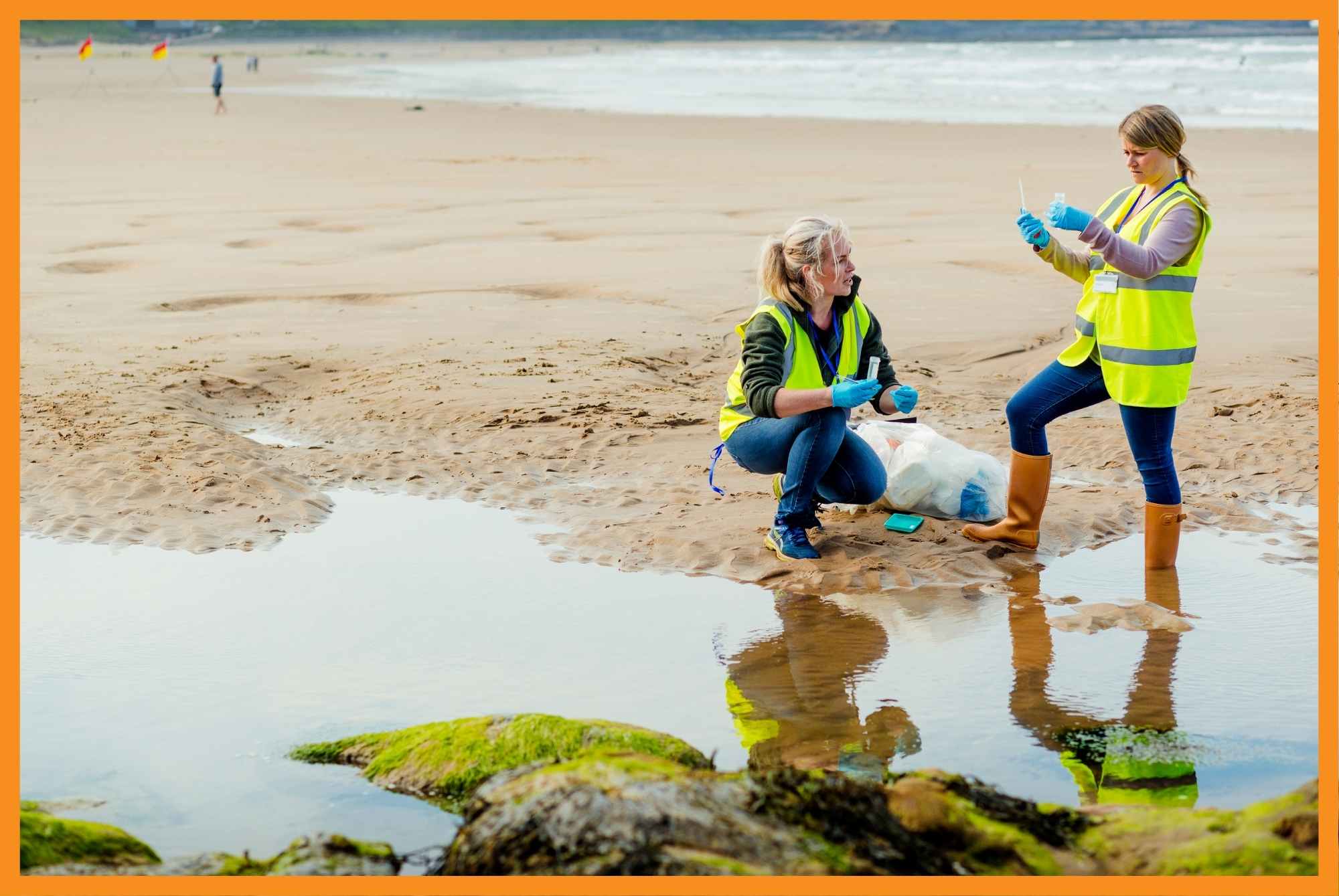 Women wearing bright green vests gather a water sample at a beach.