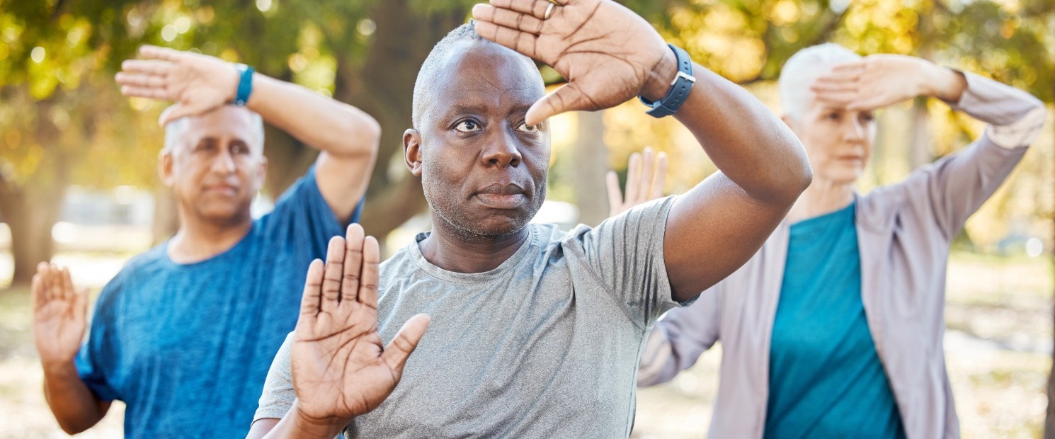 Two men and a women practice Tai Chi under the shade of trees