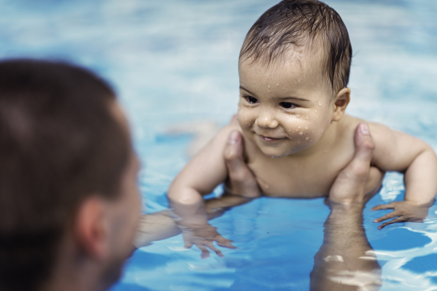 Man holds baby in a pool.